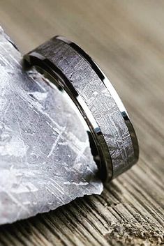 two wedding bands sitting on top of a piece of wood next to a rock and paper