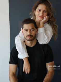 a man sitting on top of a woman's head in front of a black wall