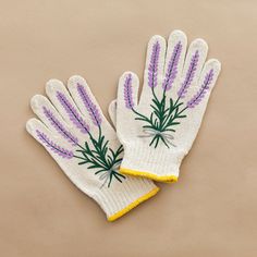 two white gloves with purple and yellow flowers on the top one has green stems on it