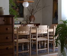 a dining room table with six chairs and a potted plant on the sideboard