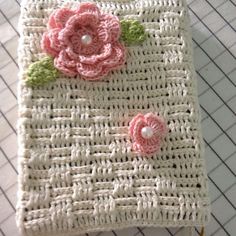 a crocheted book with pink flowers on it sitting on top of a table