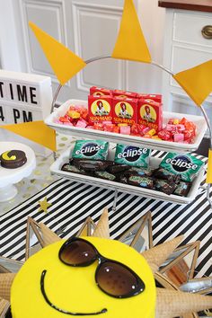 a table topped with a cake covered in chocolates and candy bar signs next to sunglasses