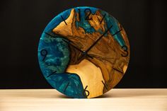 a clock made out of wood with blue and yellow paint on the face is sitting on a table