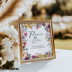 there is a sign that says flower bar on the table next to flowers and feathers