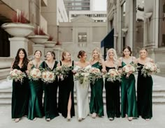 a group of women standing next to each other in front of a building holding bouquets