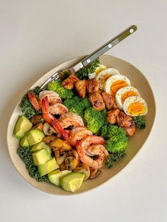 a white plate topped with shrimp, broccoli and avocado next to an egg