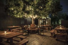 an outdoor dining area with wooden tables and benches lit up at night under a tree