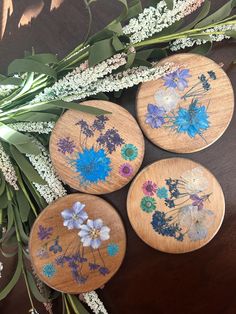 three wooden coasters with flowers painted on them sitting on a table next to greenery