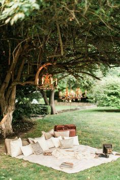 an outdoor seating area with pillows and chandelier hanging from the tree over it