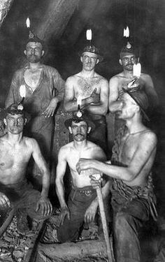 an old black and white photo of men with candles on their heads in a cave