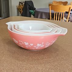 three pink bowls sitting on top of a counter next to a table with two chairs in the background