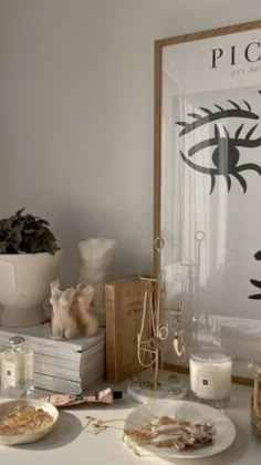 a white table topped with plates and candles next to a painting on the wall above it