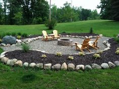 a fire pit surrounded by rocks and chairs in a grassy area with trees behind it