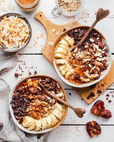 two bowls filled with granola and nuts next to spoons on a cutting board