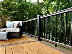 a wooden deck with black iron railings and pillows on the chair next to it