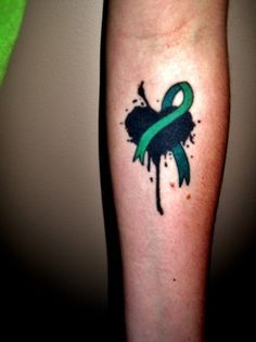 a green and black ribbon tattoo on the left leg with watercolor splatters