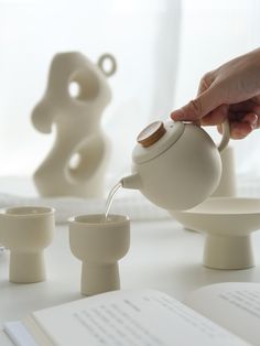 a person pours water from a teapot into small cups on a white table