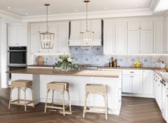 a large kitchen with white cabinets and wood flooring on the countertops, along with two stools