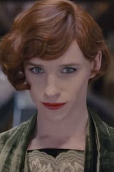 a woman with red hair and blue eyes is looking at the camera while wearing a green jacket