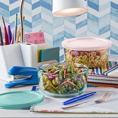 there is a bowl of salad on the table next to some pens and pencils