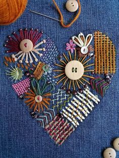 a heart made out of fabric with buttons and pins in it on a blue surface