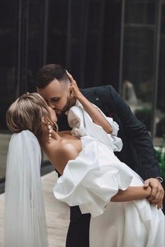 a bride and groom kissing in front of a building