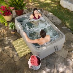 a man and woman in a hot tub on the ground next to some potted plants