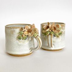 two coffee mugs with flowers on them sitting next to each other in front of a white background