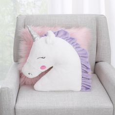 a white unicorn pillow sitting on top of a gray chair next to a pink and purple pillow