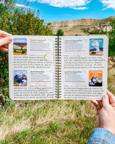 someone is holding up an open book in their hand, with mountains and trees in the background