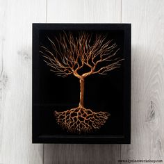 a tree with its roots in the shape of a heart on a black frame against a white wooden wall