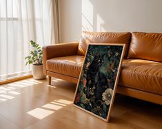 a leather couch sitting in front of a window next to a painting on the floor