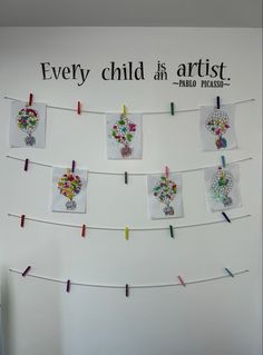 there are many pictures on the wall with clothes pins attached to it and some words above them that say every child is artist