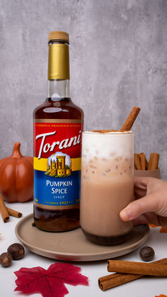 a bottle of pumpkin spice next to a cup filled with liquid and cinnamon sticks on a plate