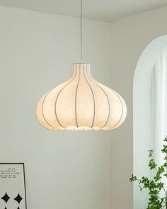 a white lamp hanging from the ceiling in a room with a potted plant next to it