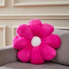 a pink flower shaped pillow sitting on top of a gray couch next to a wall