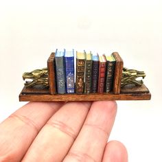 a hand holding a miniature book shelf with books on it's sides in front of a white background