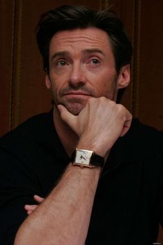 a man with a watch on his wrist looking at the camera while sitting in front of a wooden wall