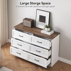 a white dresser with drawers in front of a window and a picture frame on top