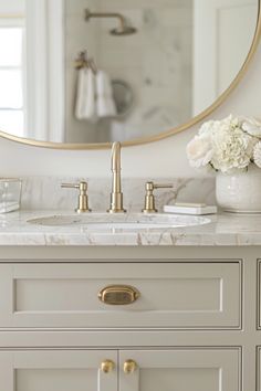 a bathroom vanity with marble counter top and gold faucet, mirror above it