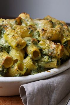 a white bowl filled with pasta and broccoli covered in sauce on top of a wooden table