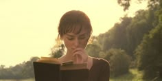 a woman is reading a book in the grass with her hand on her chin and looking down