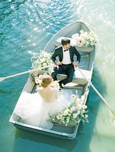 a bride and groom are sitting in a row boat on the water, dressed in tuxedo