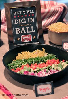 a table topped with a skillet filled with lots of veggies next to a sign