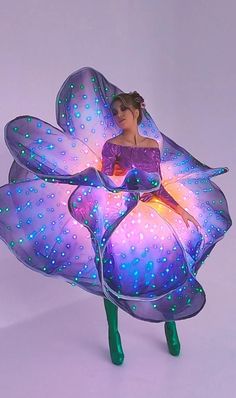 a woman in purple dress sitting on top of a large flower shaped object with blue and green lights