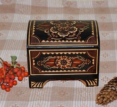 an ornate wooden box next to some berries and pine cones on a tablecloth with lace