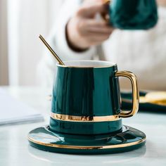 a green coffee cup with a gold rim on a saucer