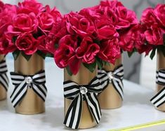 four vases with red flowers in them on a white counter top and one has a black ribbon around it