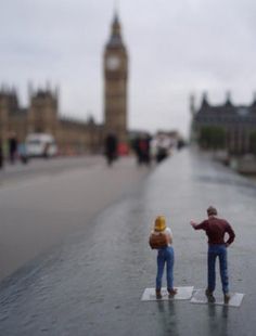 two figurines standing in the middle of a street with big ben in the background