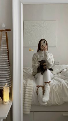 a woman sitting on top of a bed holding a cat and taking a selfie